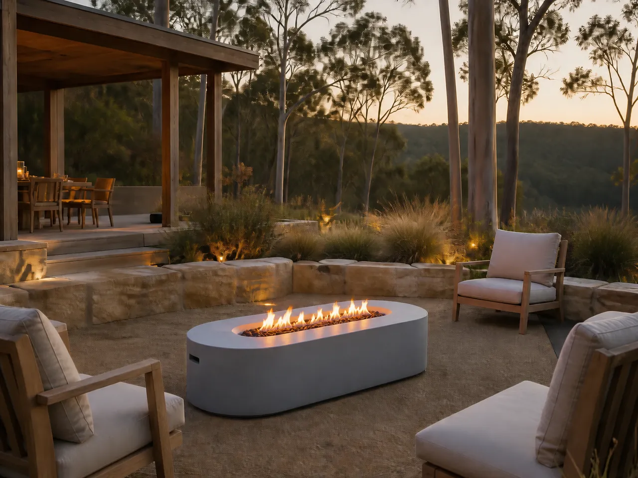 Orion Modern Oval Gas Fire Pit Table with a linear flame, set on a stone patio with wooden lounge chairs at dusk.